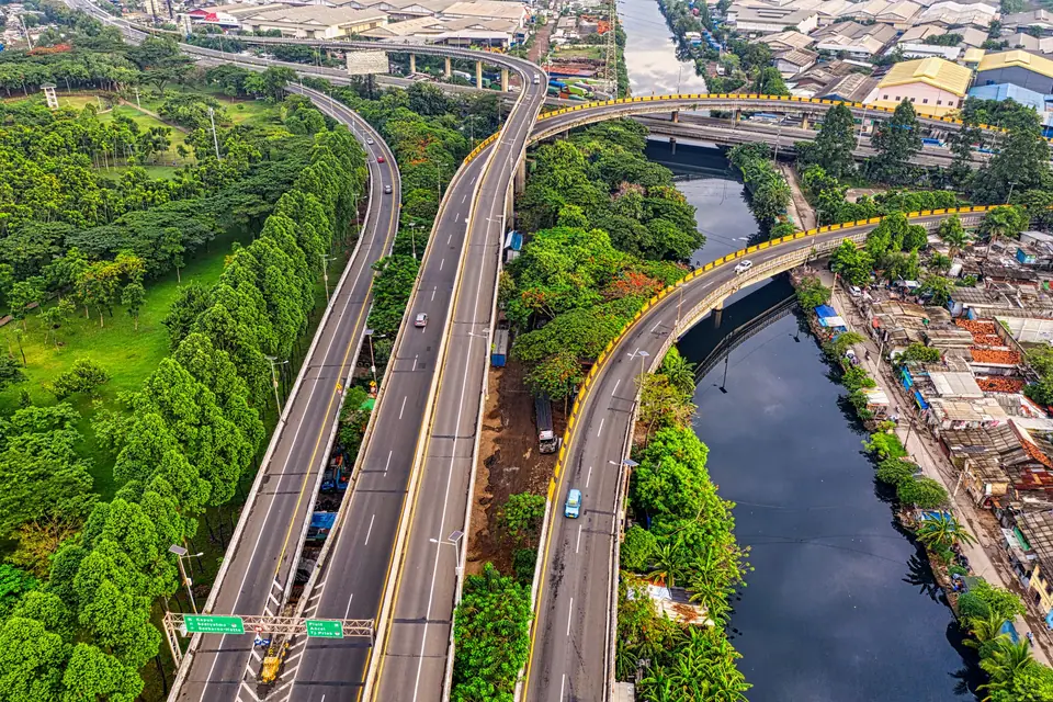 Foto udara jalan layang dan jalan tol dengan sungai dan pepohonan
